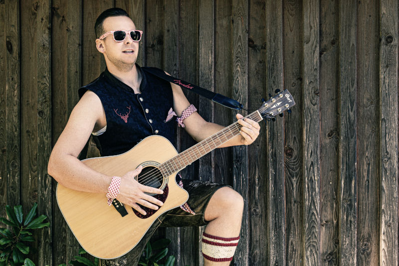 Andreas Gabalier Double Tobi mit Gitarre und Holz Hintergrund